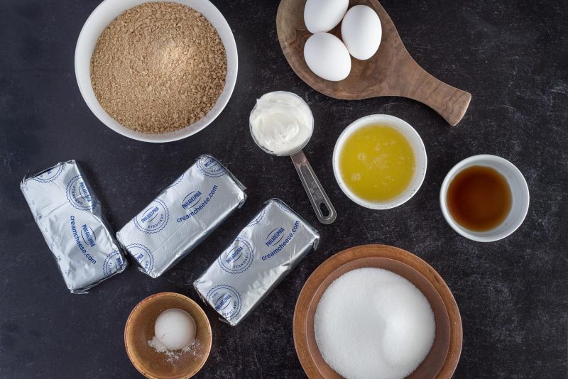 Ingredients for an 8-inch Instant Pot cheesecake, including sugar, flour, cream cheese, sour cream, melted butter, vanilla, eggs, and graham cracker.