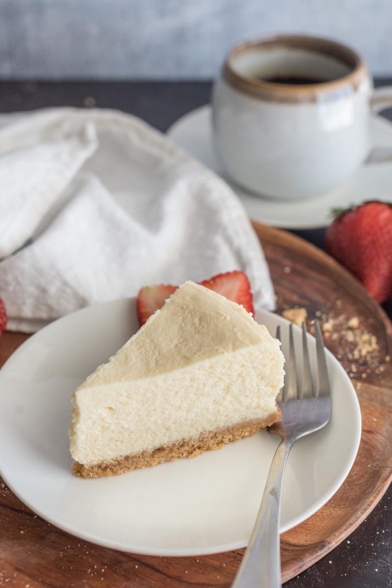 A slice of 8 inch Instant Pot cheesecake on a white plate with a fork and sliced strawberries.