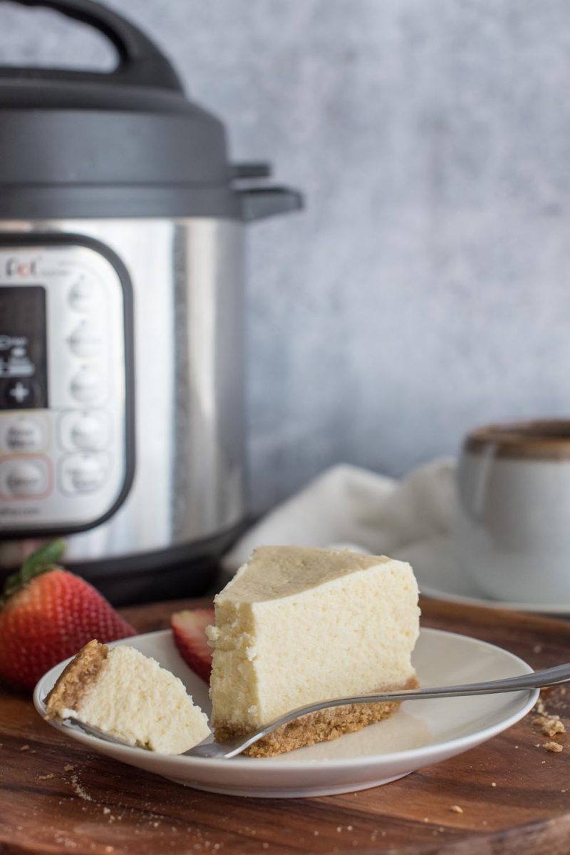 A slice of cheesecake from an 8 inch cheesecake on a plate and placed in front of an Instant Pot.