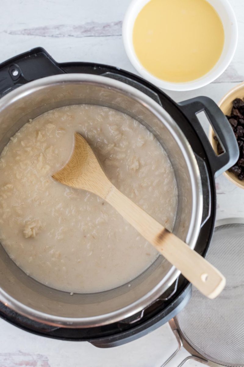 Rice pudding after the pressure cooking cycle in an Instant Pot, with egg mixture in a white bowl waiting to be mixed in.