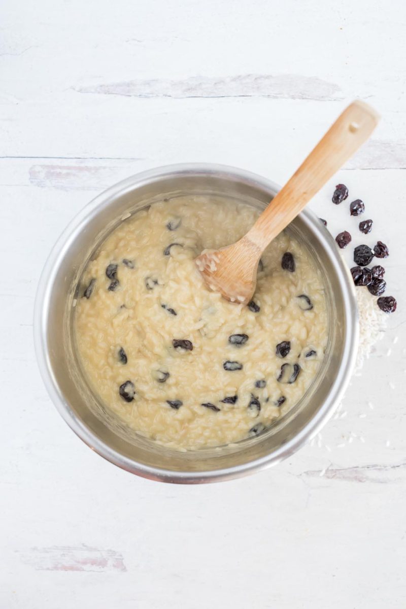 Overhead picture of rice pudding in an Instant Pot inner pot stirring in the dried cherries with a wooden spoon.