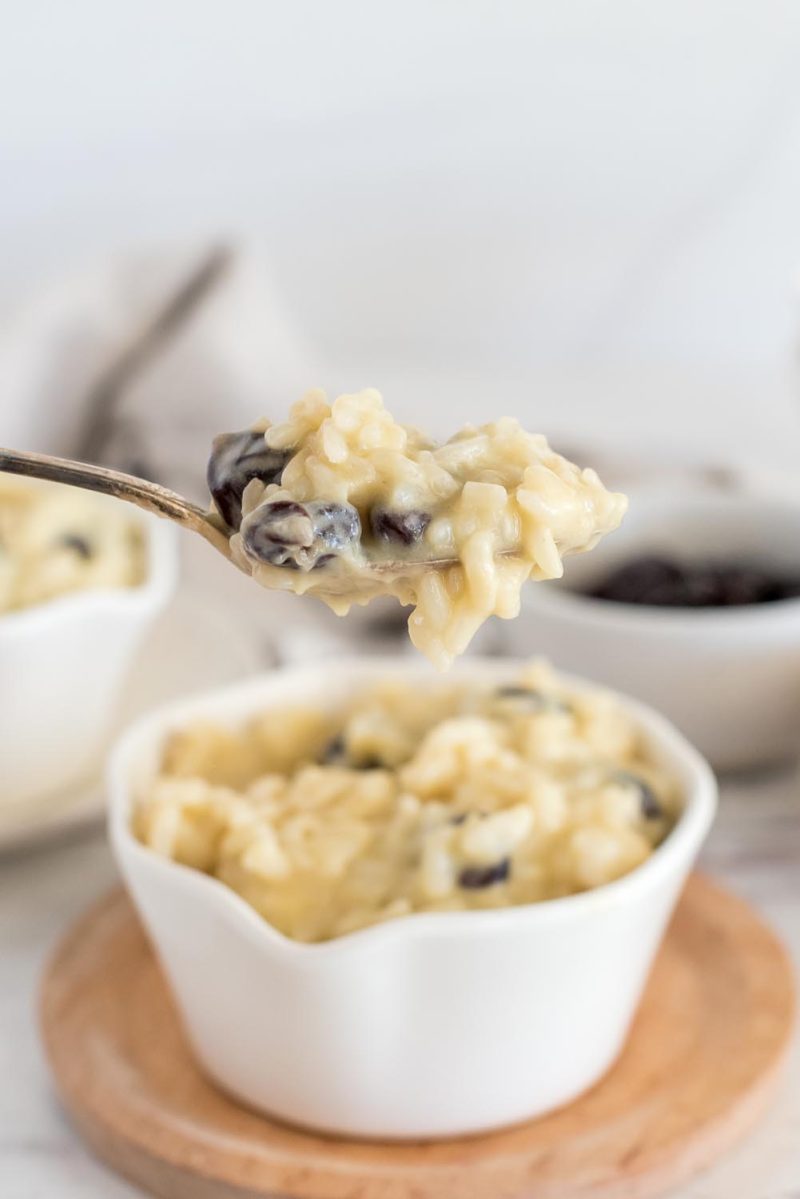 A spoon full of Instant Pot rice pudding made with dairy free almond milk and dried cherries, over a white bowl filled with rice pudding.