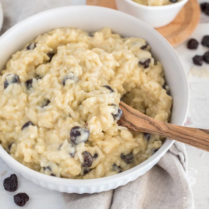 A white bowl with Instant Pot dairy free rice pudding with rice cherries, and a wooden spoon.