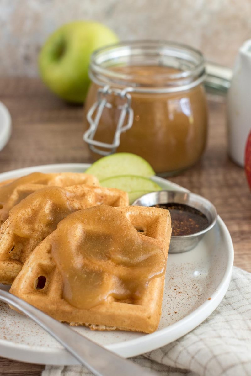 Waffles topped with Instant Pot apple butter on a white plate with a jar of apple butter in the background.