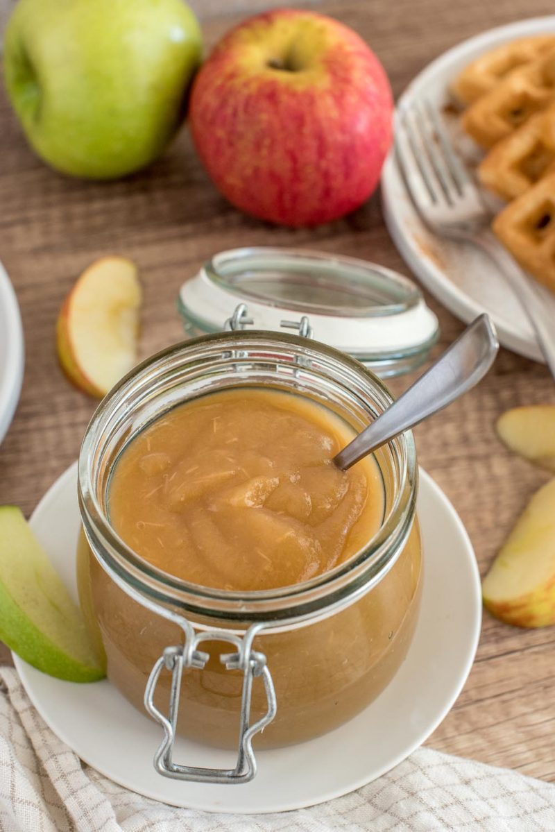 Instant Pot apple butter in a glass jar with waffles in the background.