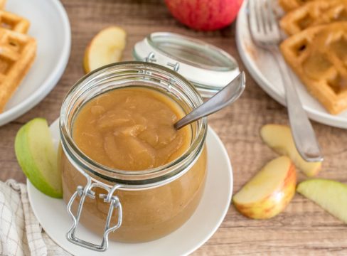 Instant Pot apple butter in a glass jar with waffles in the background.