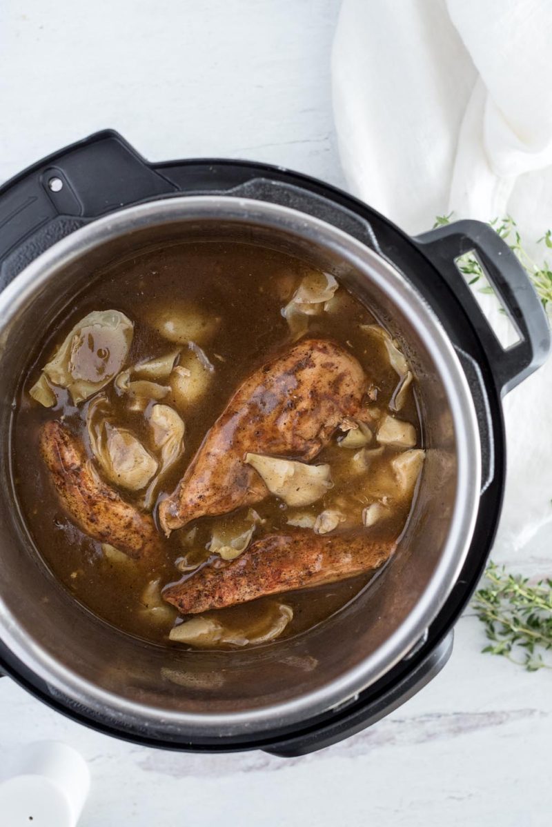 An overhead shot of the chicken after cooking in the Instant Pot, with the artichoke pieces floating on top