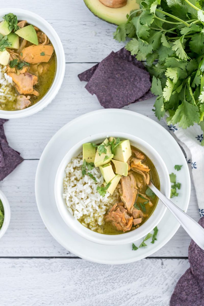 Overhead picture of Instant Pot asopao served in a white bowl with rice and avocado, with fresh cilantro and a second bowl of asopao in the background.