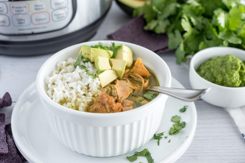 A white bowl filled with asopoa, white rice, and avocado and placed in front of an Instant Pot with fresh cilantro and sofrito in the background.