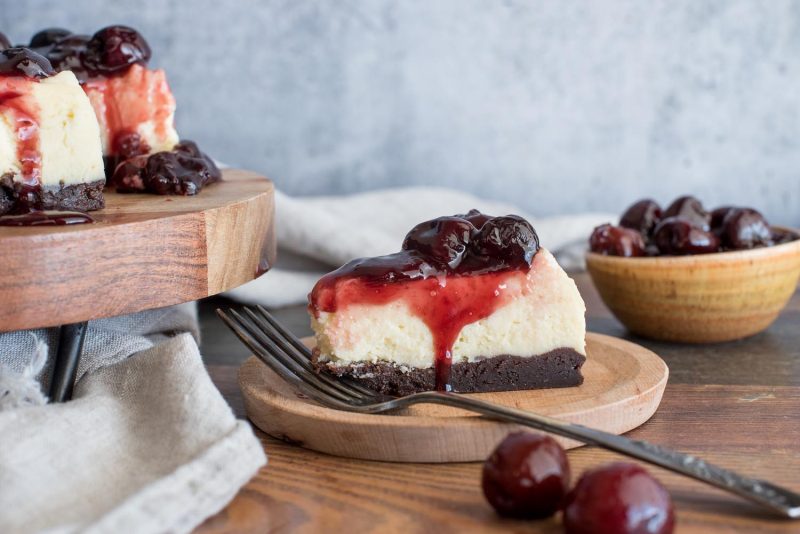 A slice of Instant Pot Black Forest cheesecake with a bowl of cherries in the background.