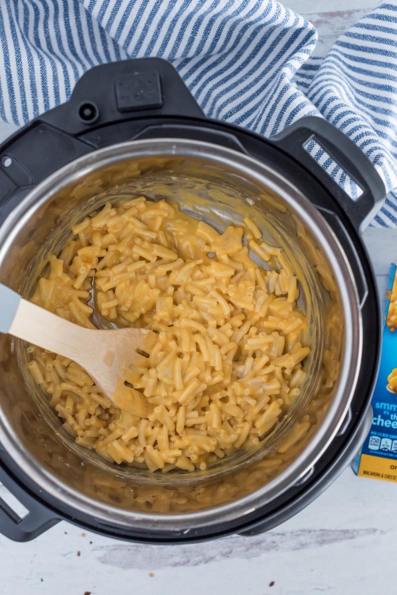 An overhead shot looking down into the Instant Pot after the pasta has been cooked and after the cheese packet has been stirred in. The macaroni and cheese looks creamy next to a wooden spoon.
