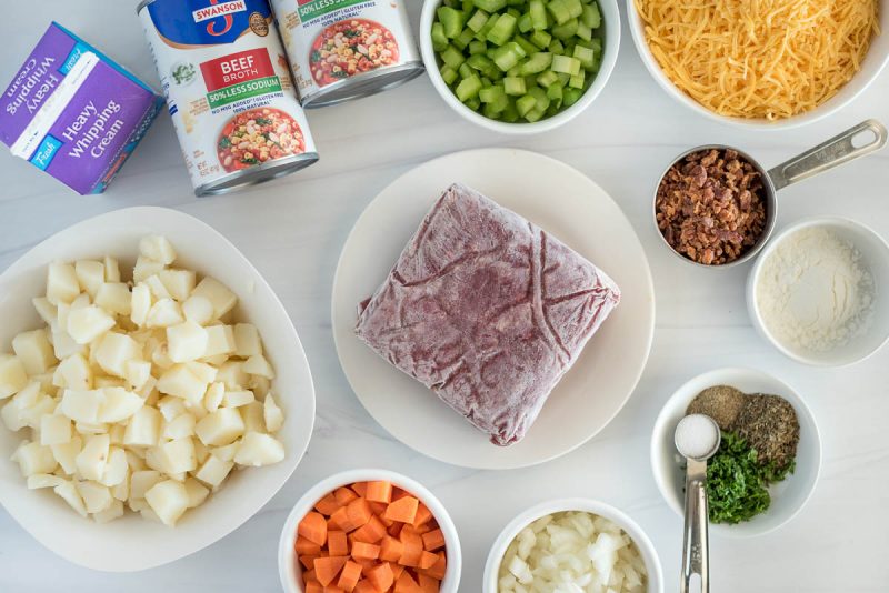 Ingredients for Instant Pot cheeseburger soup, including frozen beef, carrots, onions, spices, corn starch, celery, broth, cream, potatoes, and cheese.