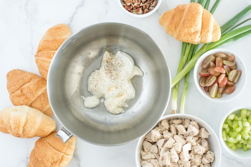 Preparing to mix the Instant Pot chicken sandwiches with mayonnaise and lemon juice in the bowl, with chicken, celery, grapes, green onions, pecans and croissants in the background.