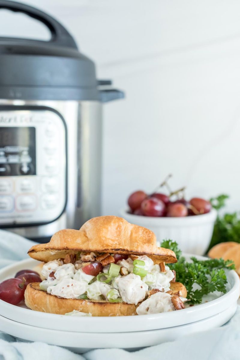 A chicken salad sandwich served on croissant and place on a white plate in front of an Instant Pot.