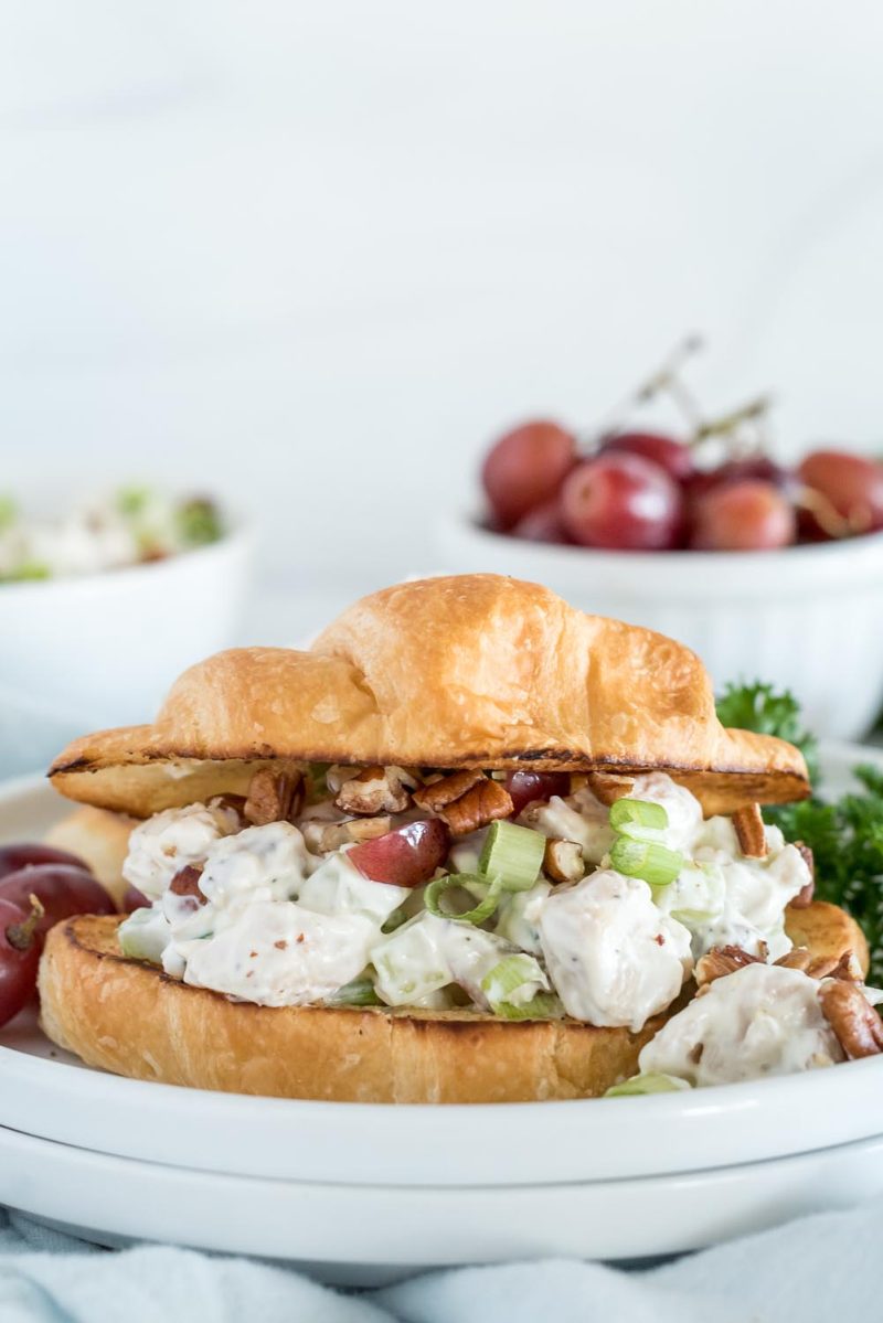 Instant Pot chicken salad sandwiches served on croissants and placed on a white plate with parsley and grapes.
