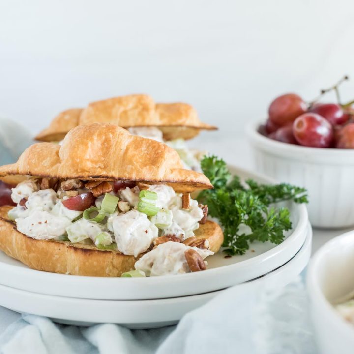 Instant Pot chicken salad sandwiches served on croissants and placed on a white plate with parsley and grapes.