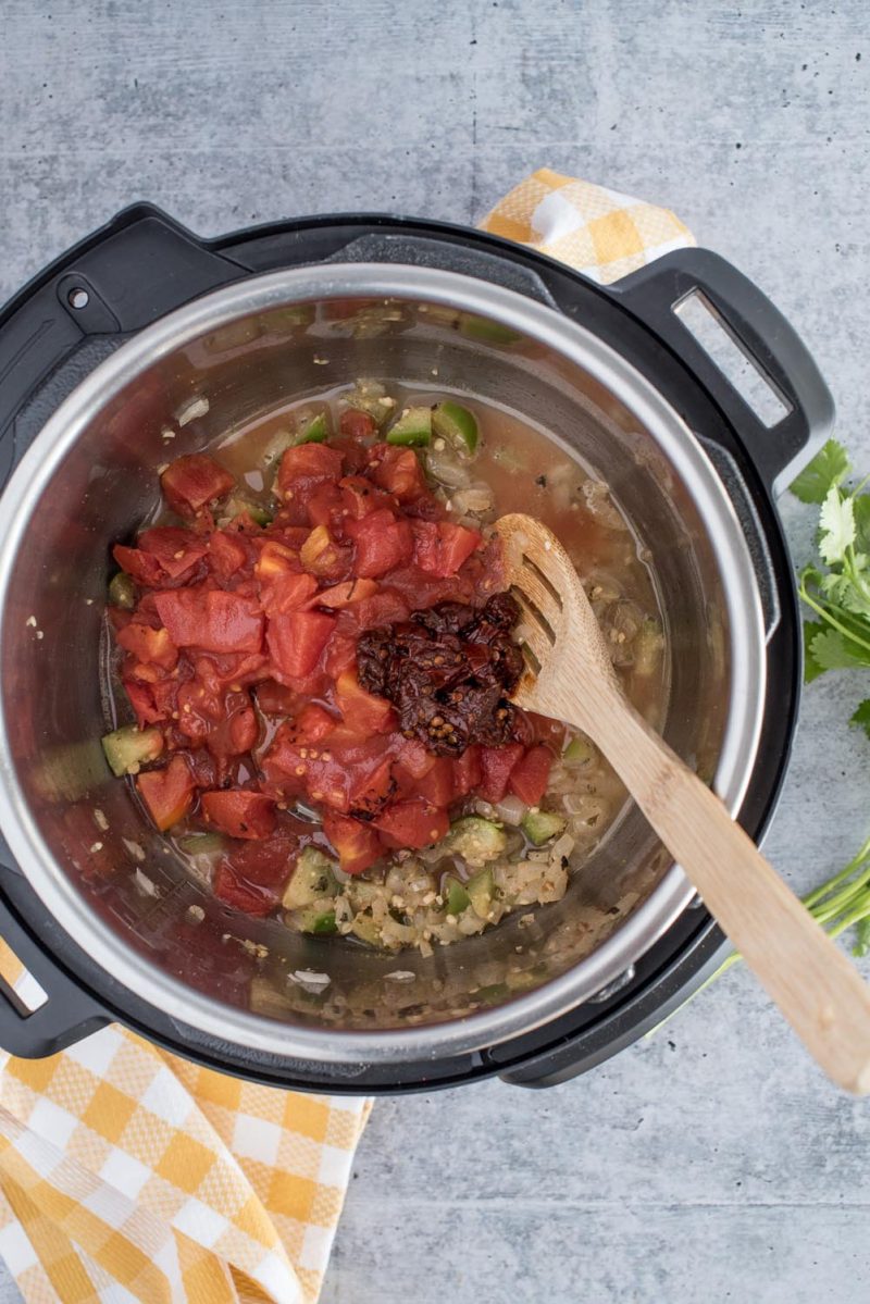 an overhead vertical shot of tomatoes and adobo sauce added to the pressure cooking pot.