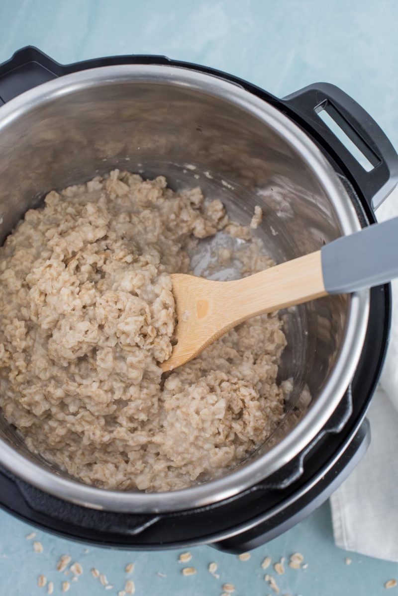 An overhead picture of oatmeal that has been cooked in an Instant pot with a wooden spoon for mixing and serving.