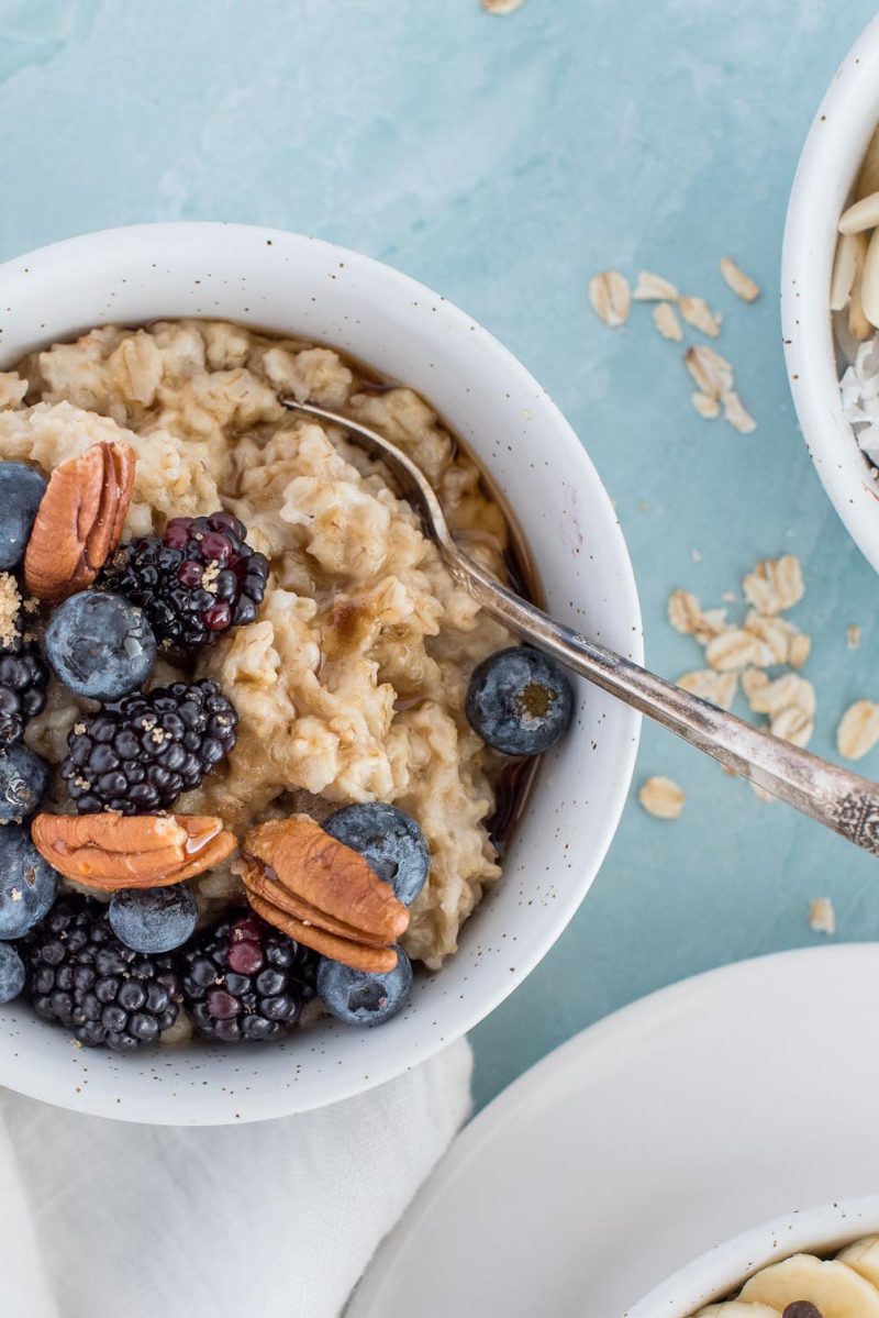 An overhead picture of Instant Pot oatmeal served in a white bowl and topped with blackberries, blueberries and pecans, with more oatmeal in the background.
