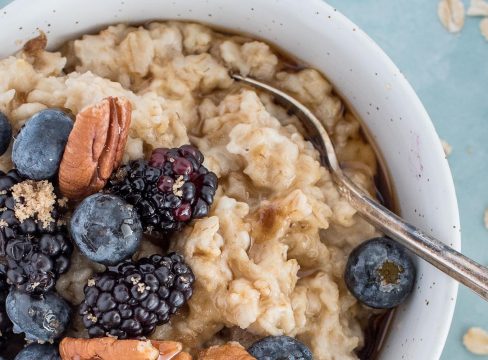 A close up picture of Instant Pot oatmeal served in a white bowl and topped with blackberries, blueberries and pecans.