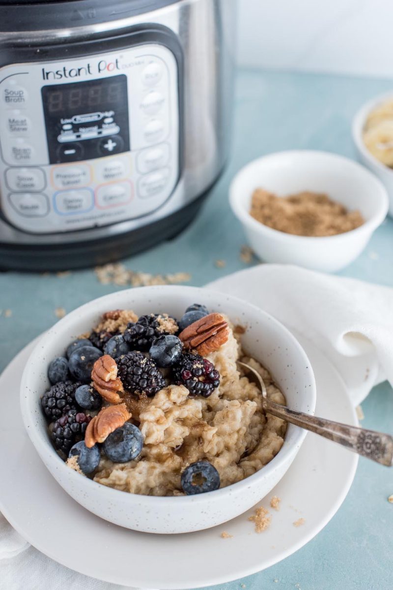 A white bowl filled with oatmeal topped with blackberries, blueberries, and pecans, placed in front of an Instant Pot, with brown sugar in the background.