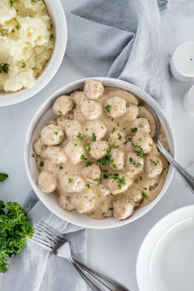 An overhead picture of Instant Pot Swedish Meatballs and gravy in a serving bowl, and mashed potatoes in the background.