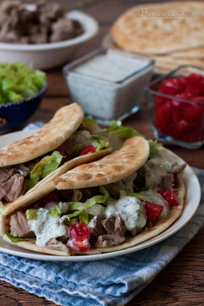 Greek pork taco recipe, featuring two pitas filled with lettuce, pork, tomatoes, and sauce, on a white plate placed on a blue and white placemat.  from Pressure Cooking Today