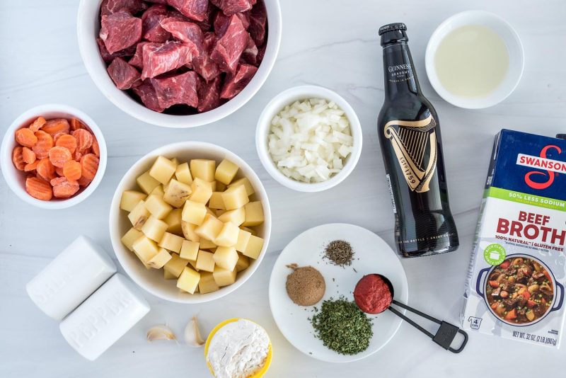 Ingredients for Instant Pot Guinness stew including a bottle of Guinness Draught beer, beef broth, spices, onions potatoes, carrots garlic, and beef.