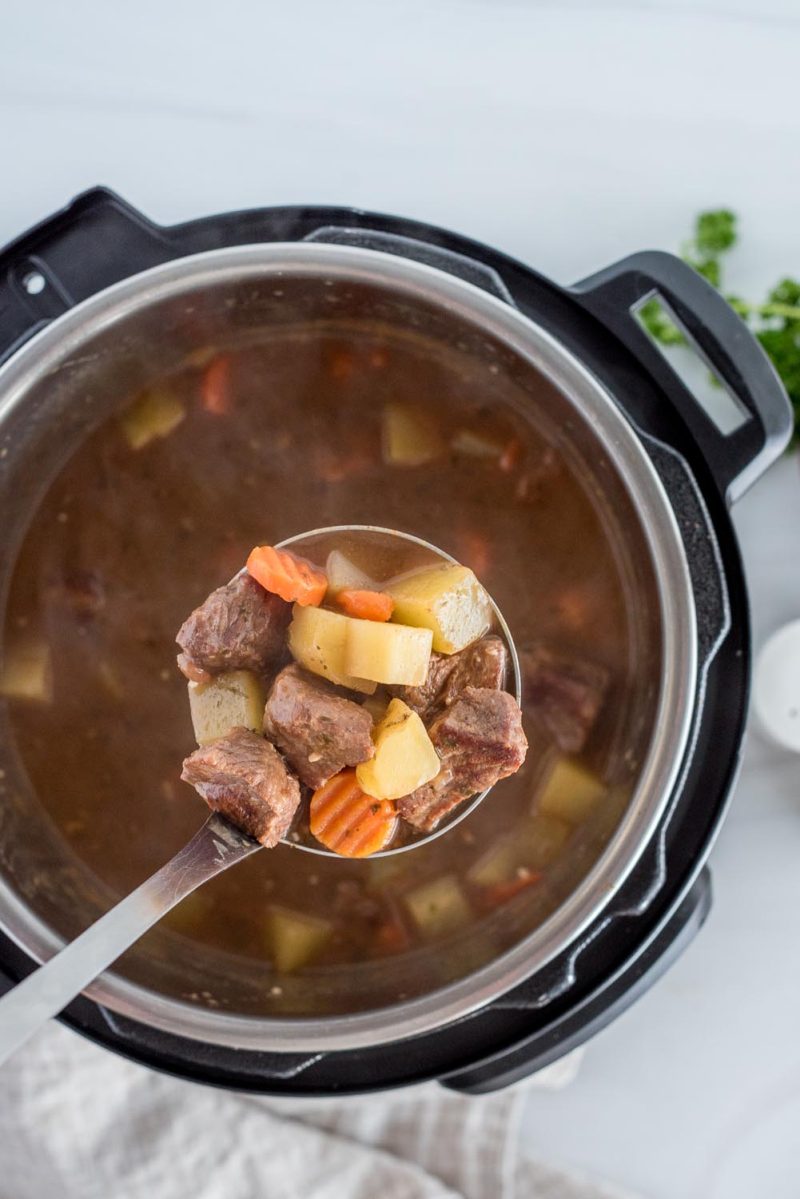 An overhead picture of Guinness stew cooking in an Instant Pot with a label scooping out beef, potatoes, and carrots.