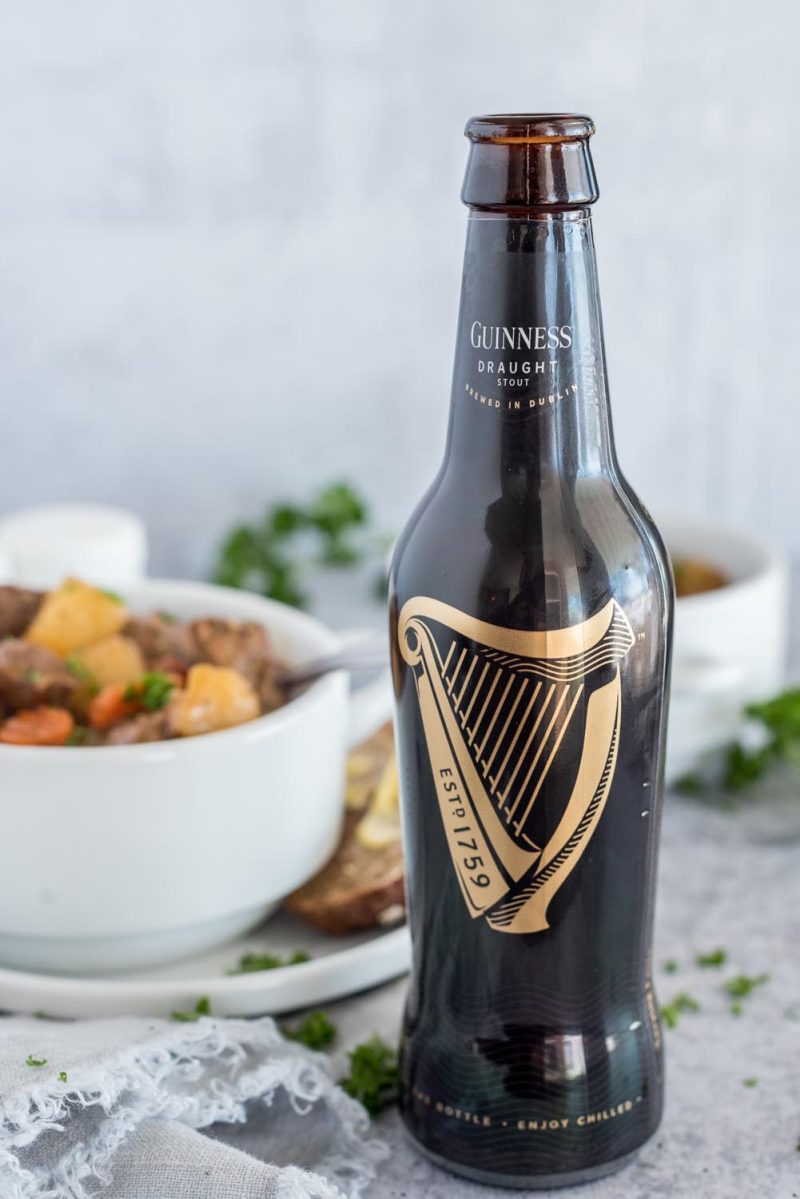 A bottle of Guinness beer with a bowl of Instant Pot Guinness stew in the background.