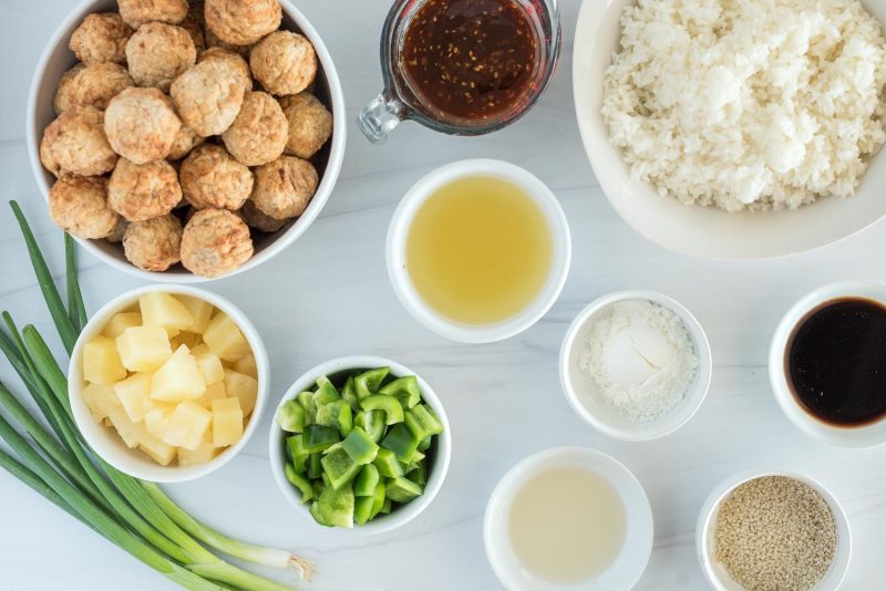 Ingredients for Instant Pot Hawaiian meatballs, including green onion, bell peppers, pineapple, sesame seeds, teriyaki sauce, soy sauce, pineapple juice, corn starch and cooked white rice.