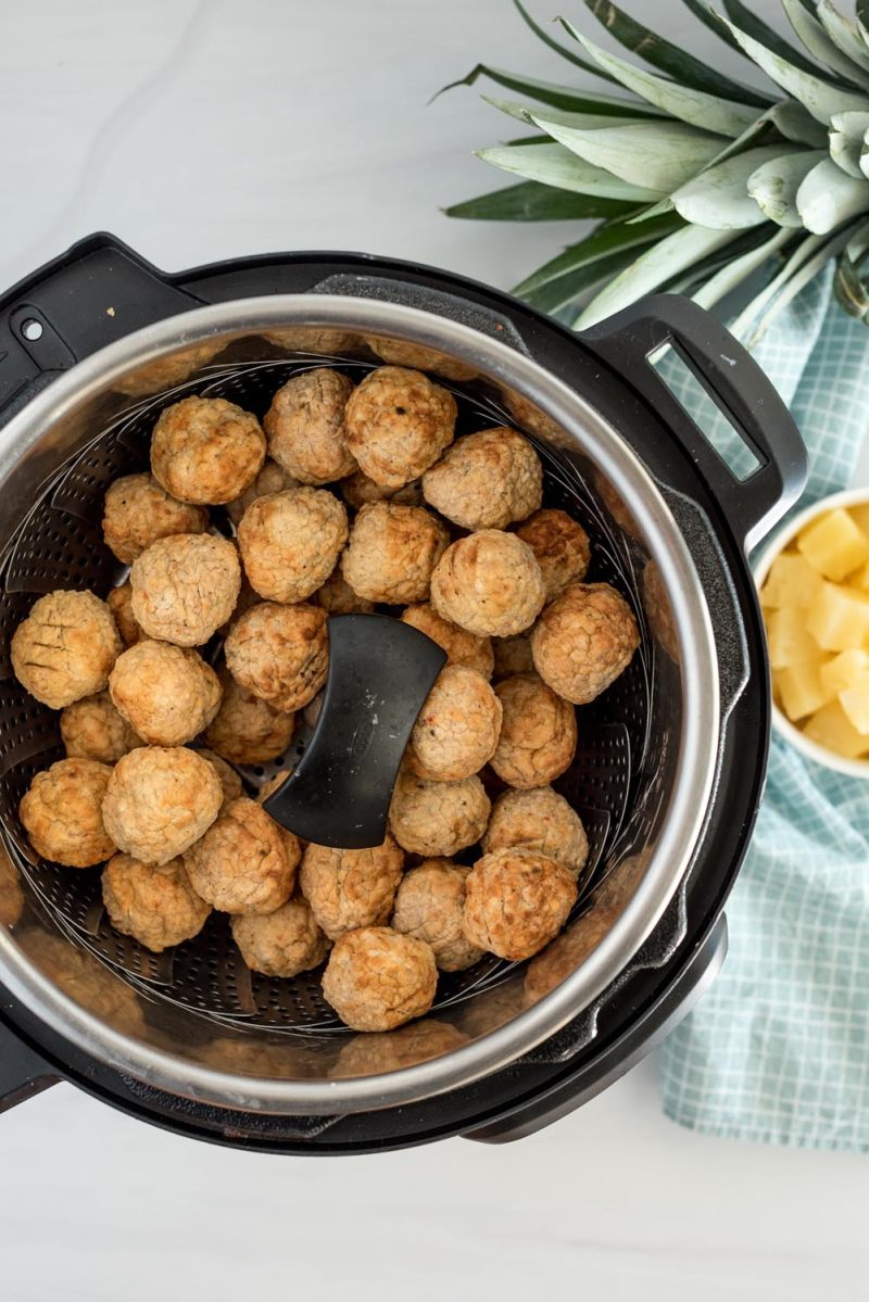 an overhead picture cooking Hawaiian meatballs in a steamer basket in an Instant Pot.
