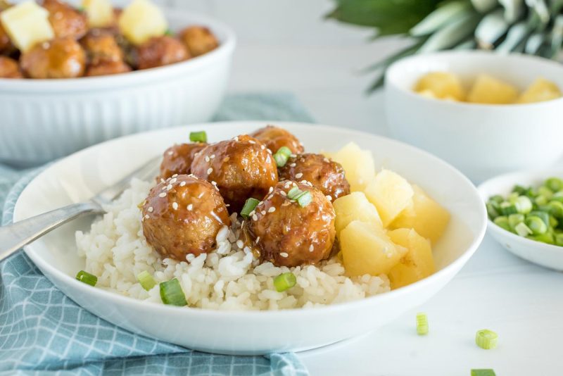 Close up picture of Instant Pot Hawaiian meatballs served over rice, and topped with sesame seats and green onions.