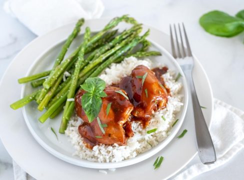 Instant Pot honey garlic chicken plated on white rice and asparagus, topped with fresh parsley.