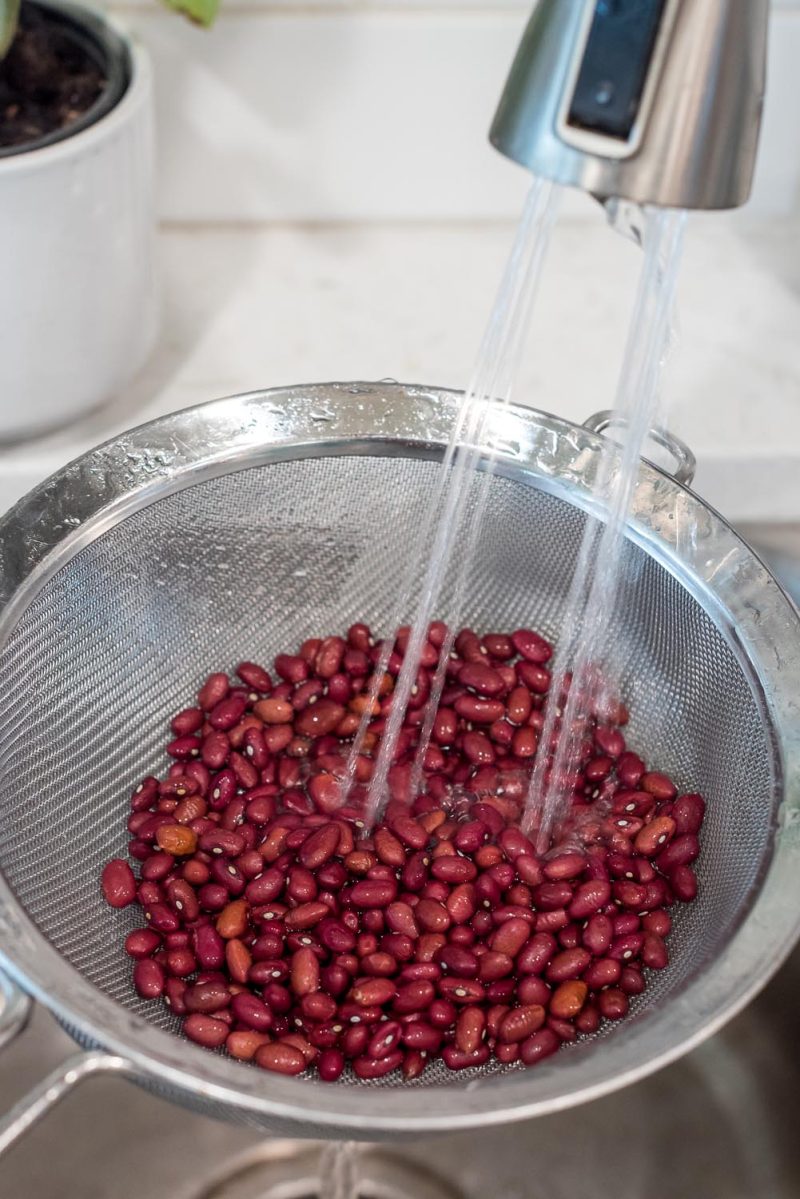 Rinsing dried kidney beans in a wire mesh strainer over a sink.