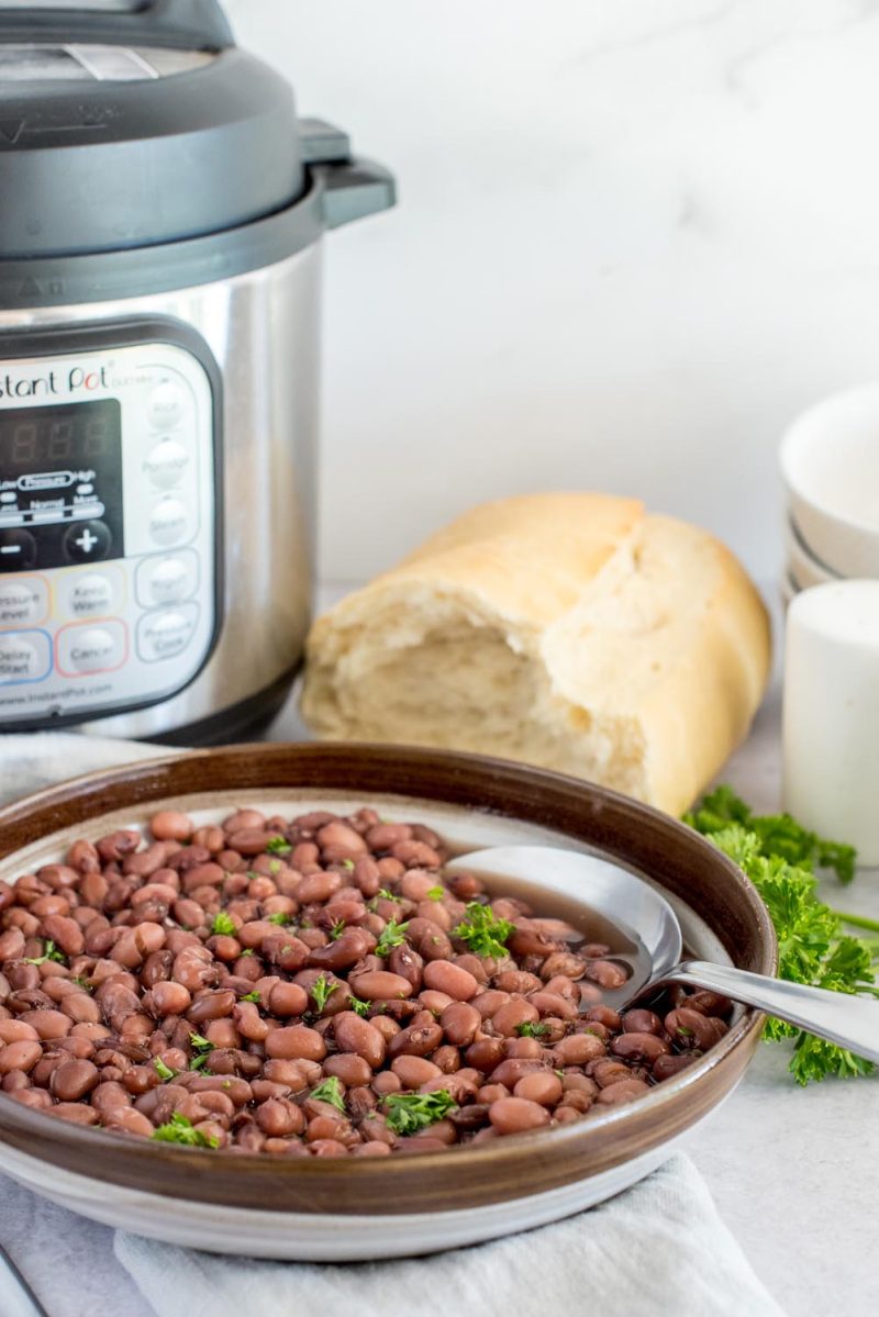 A bowl of kidney beans topped fish fresh parsley, placed in front of an Instant Pot.