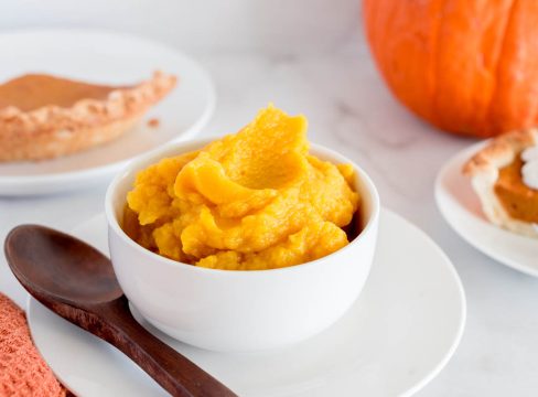 Instant Pot pumpkin in a white bowl with a pumpkin pie off to the side and a pumpkin in the background.