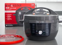 Instant Pot Rio Wide Plus with the extra gasket and trivet that is included, placed in front of the product box.