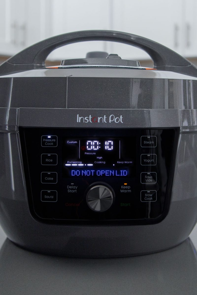 Picture showing the front of the Instant Pot Rio Plus Wide in the middle of pressure cooking. The display features a flashing bar in the Cooking display, with 10 minutes on the custom cook time setting.