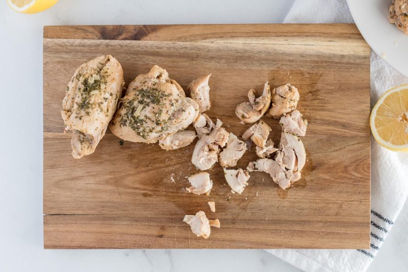 Chopping cooked chicken thighs on a wooden cutting board.