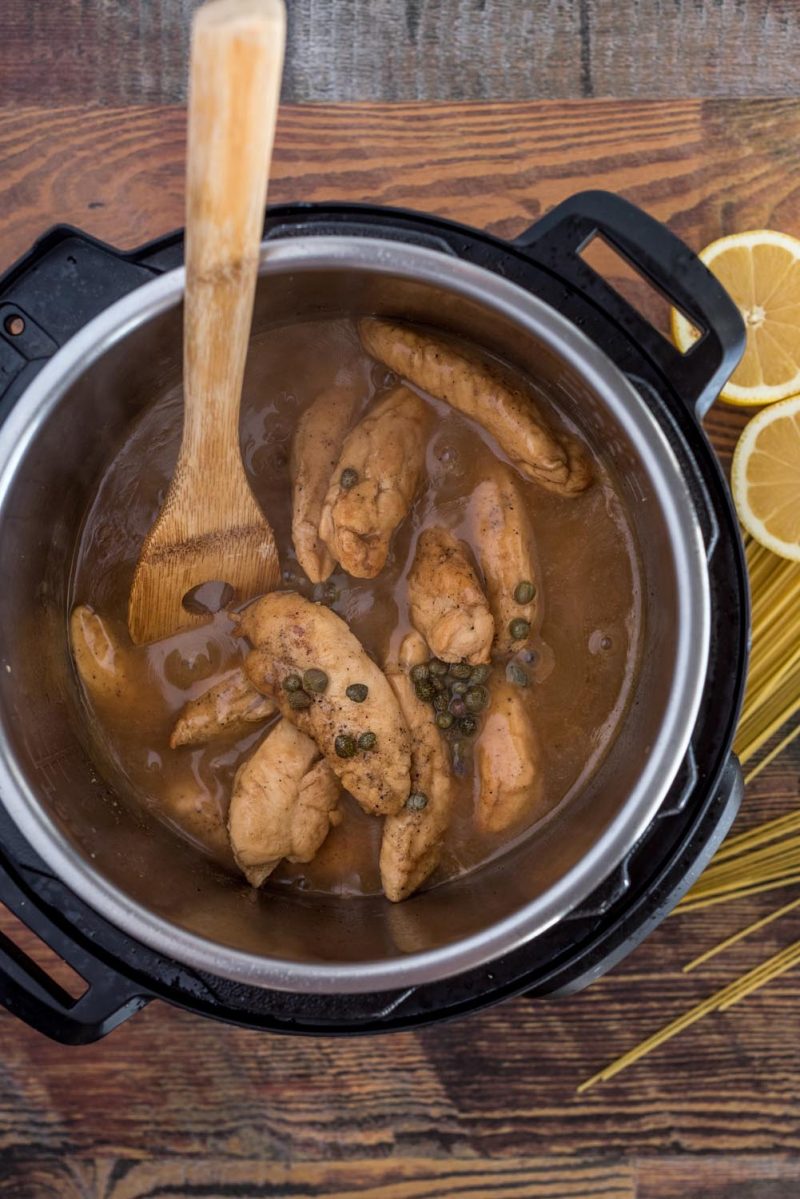 Overhead picture of lemon chicken piccata cooked inside an Instant Pot with a wood spoon used to stir.