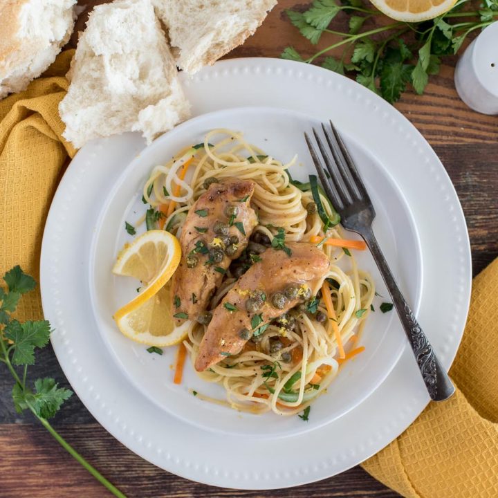 Overhead picture of Instant Pot lemon chicken piccata served on a white plate with pasta,carrots, and zucchini.
