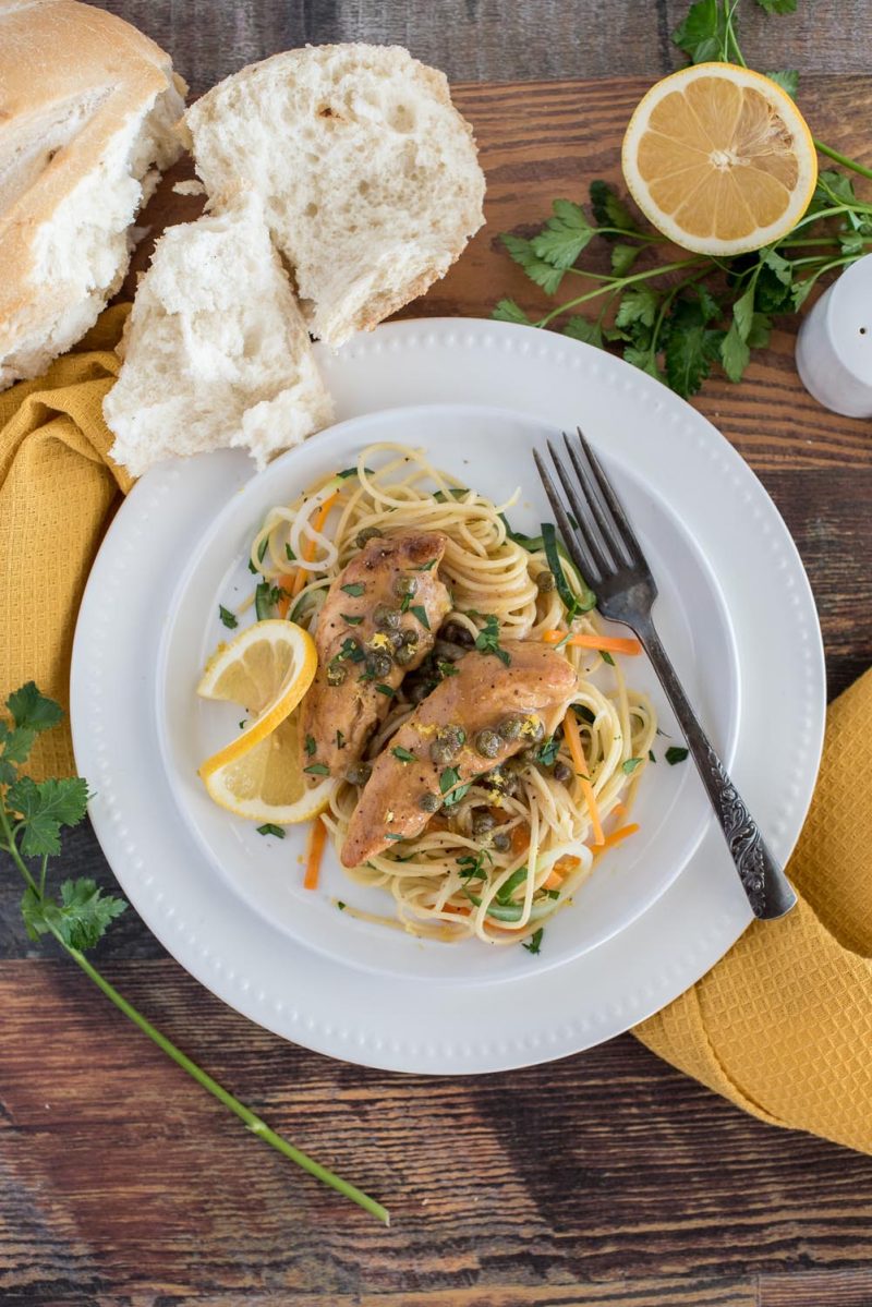 Overhead picture of Instant Pot lemon chicken piccata served on a white plate with pasta,carrots, and zucchini.