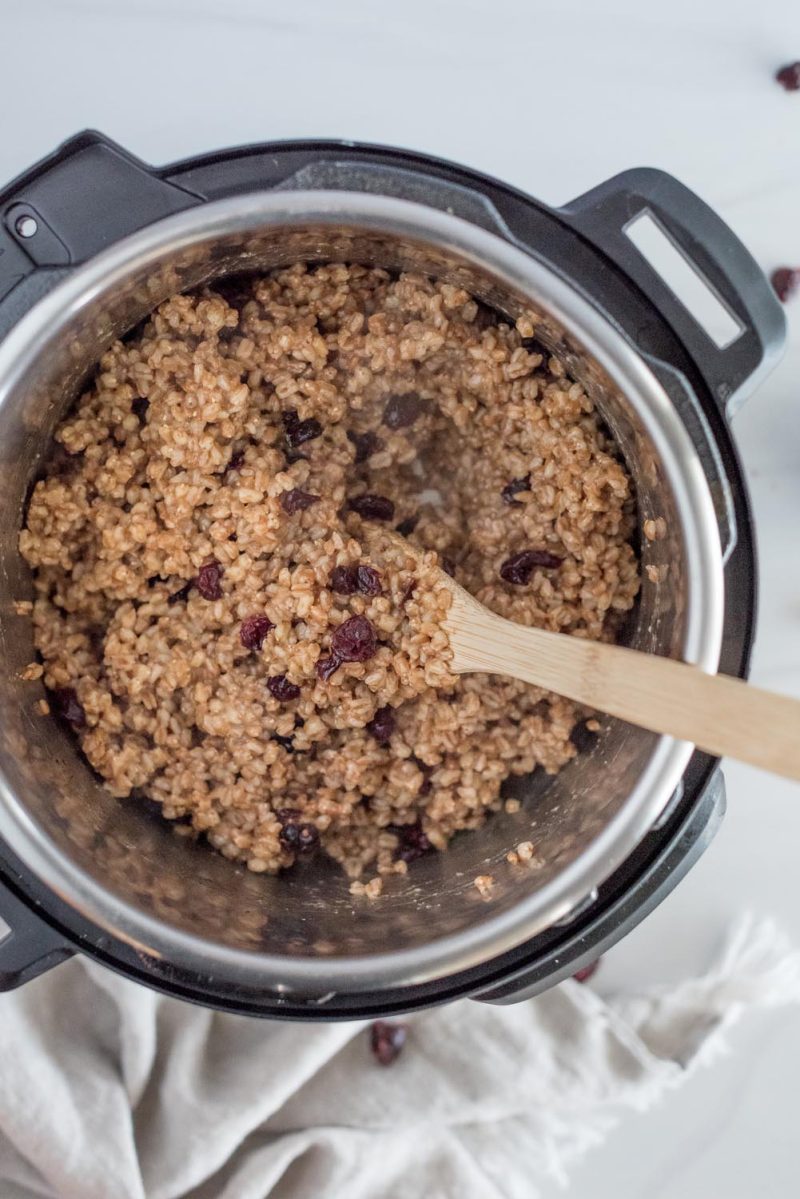 An overhead picture of cooked lemon cherry farro with a wooden mixing spoon, inside an Instant Pot.