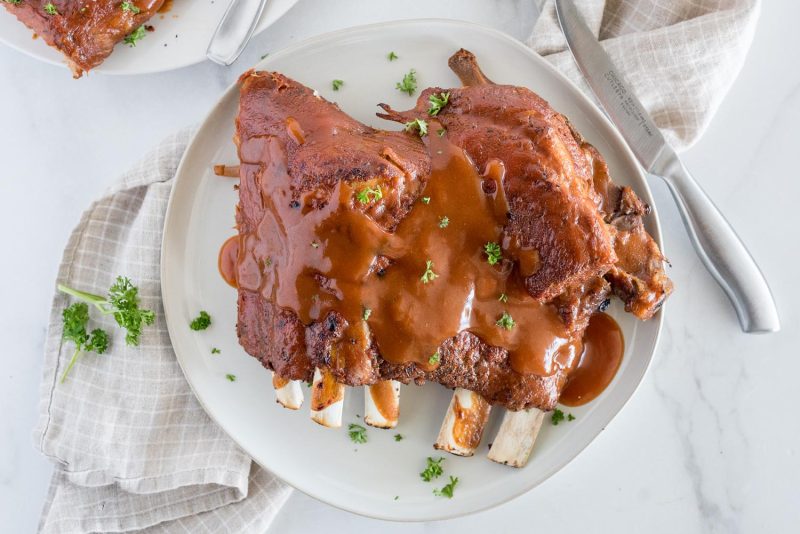 An overhead picture of a white plate with about half a rack of Memphis style ribs smothered in homemade BBQ sauce that were cooked in an Instant Pot.