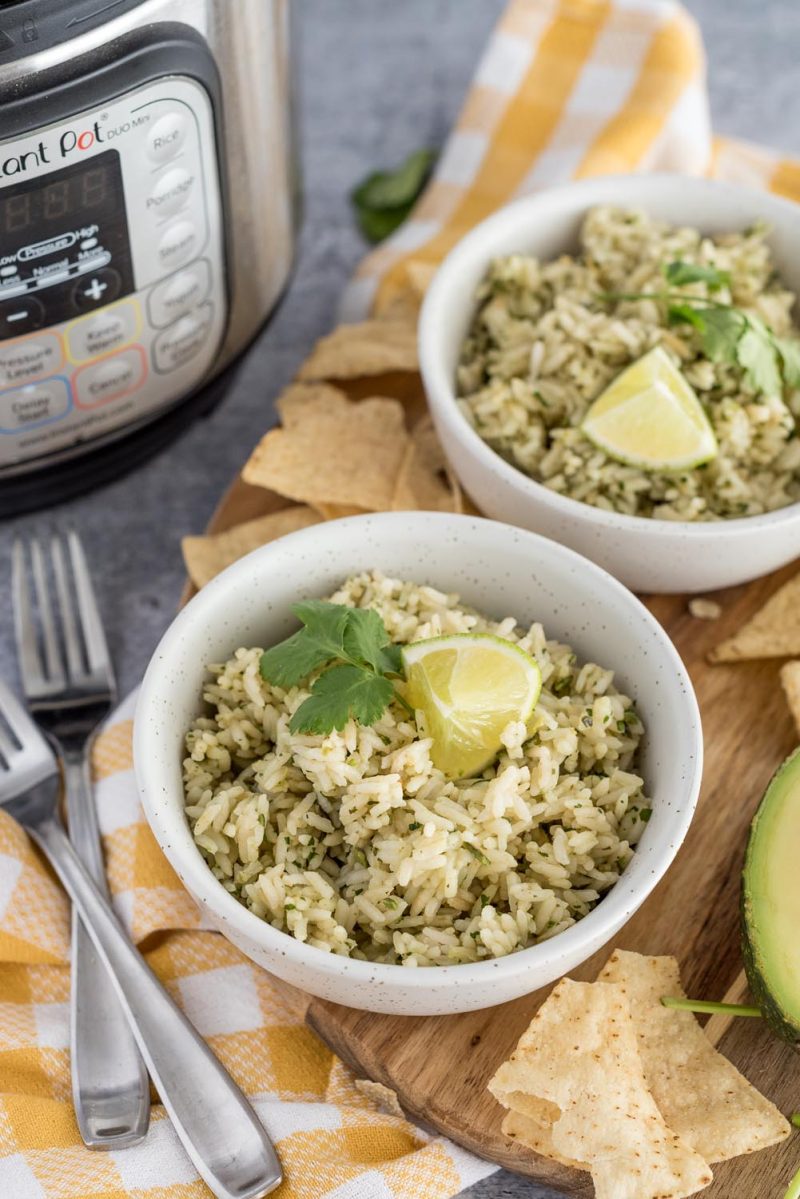 Picture of two bowls of green salsa rice with lime wedges and fresh cilantro on top, placed in front of an Instant Pot.