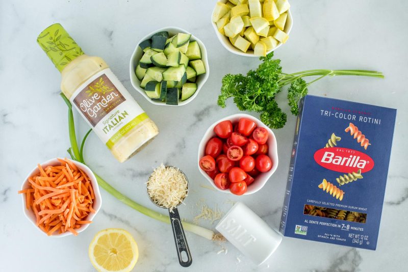 Ingredients for making Instant Pot pasta salad, including rotini noodles, cherry tomatoes, fresh parsley, yellow squash, cucumber, Italian dressing, matchstick carrots, green onion, lemon, parmesan, and salt.