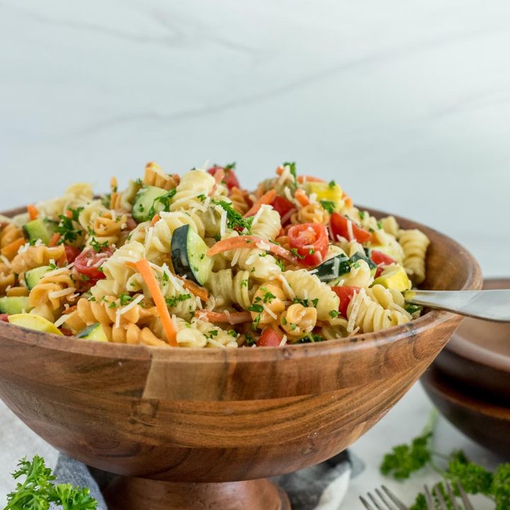 Picture of Instant Pot pasta salad with rotini, sliced cherry tomatoes, zucchini, cucumber, parmesan, and fresh parsley, in a large wooden serving bowl.