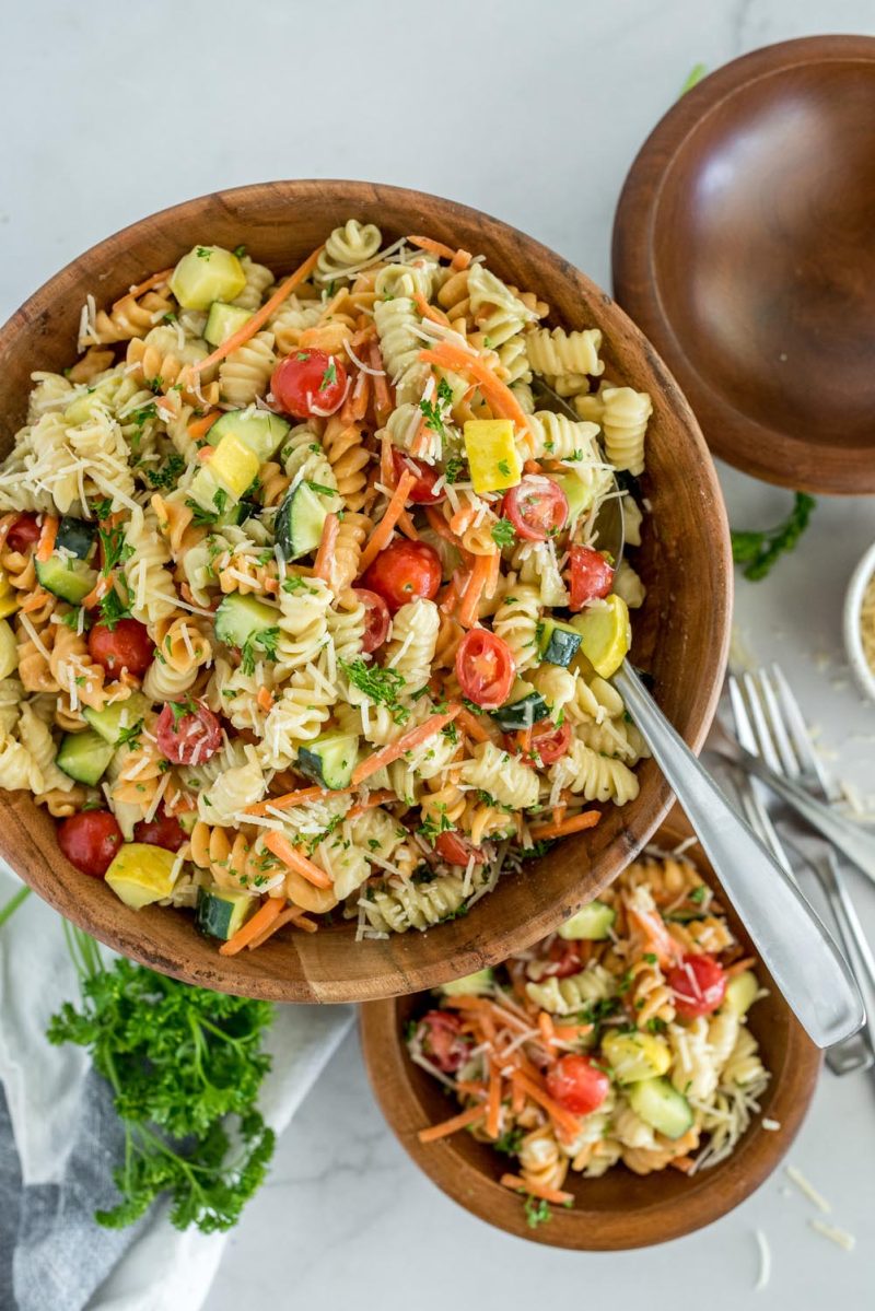 Overhead Picture of Instant Pot pasta salad with rotini, sliced cherry tomatoes, zucchini, cucumber, parmesan, and fresh parsley, in a large wooden serving bowl.