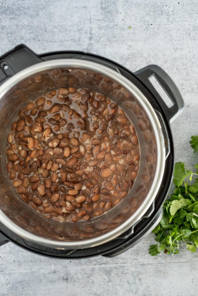 An overhead picture of cooked pinto beans in an Instant Pot with cilantro to the side.
